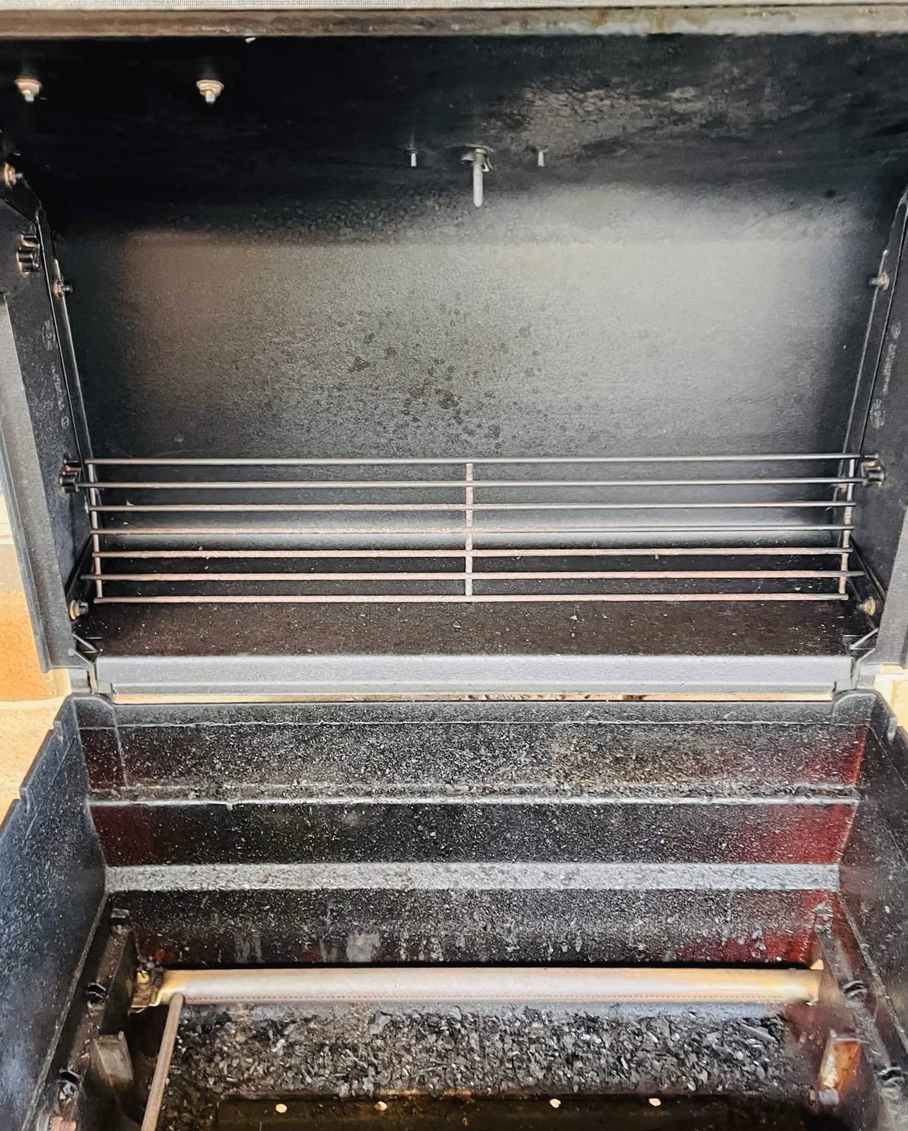 Gas BBQ with the hood open, showing grill bars and a base heavy with carbon and grease