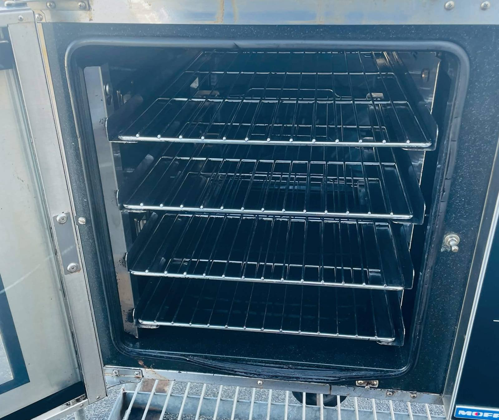 Commercial convection oven with the door open, showing clean wire shelves and a degreased cavity