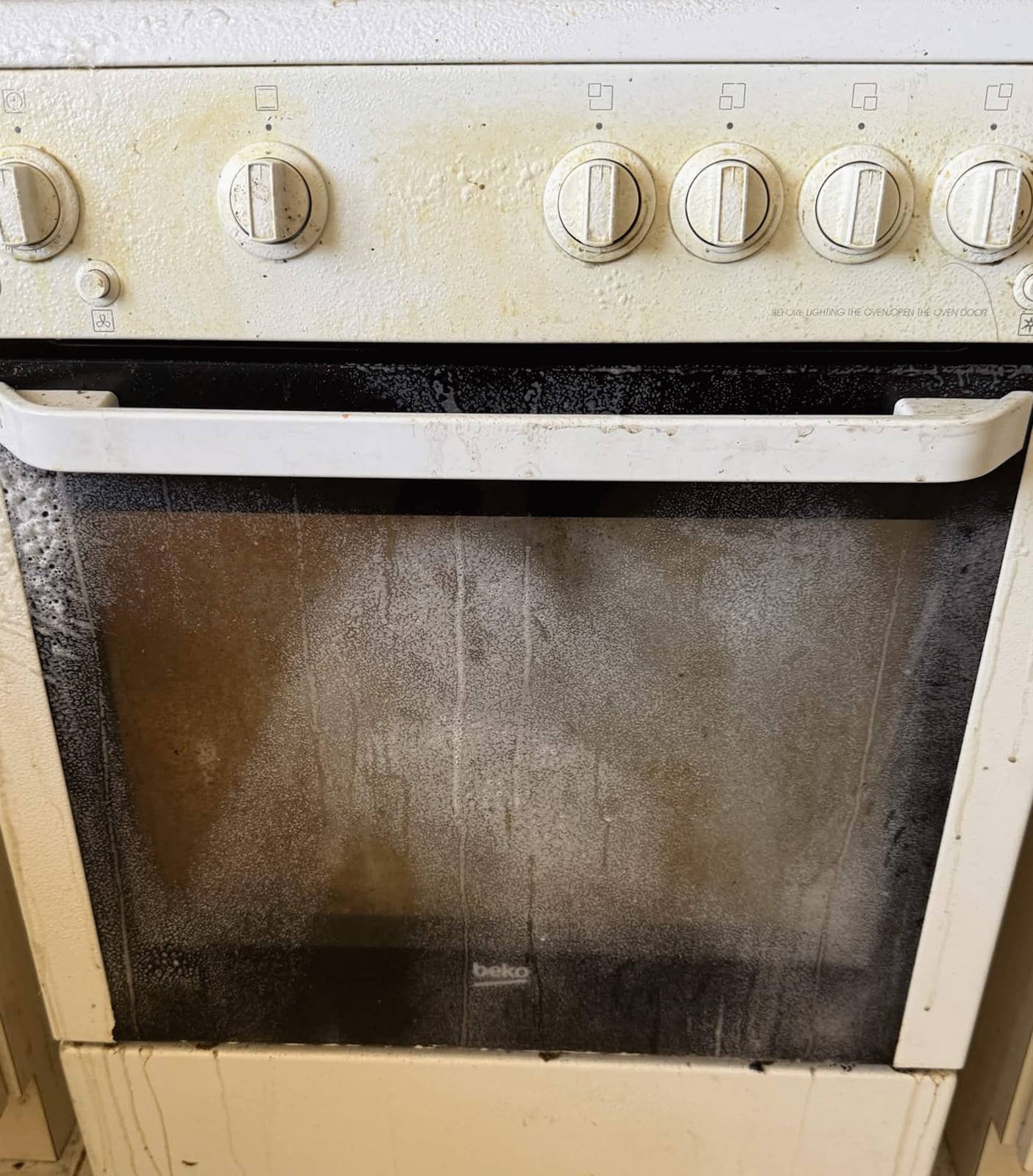 White freestanding cooker with a darkened oven door and grease marks around the control knobs