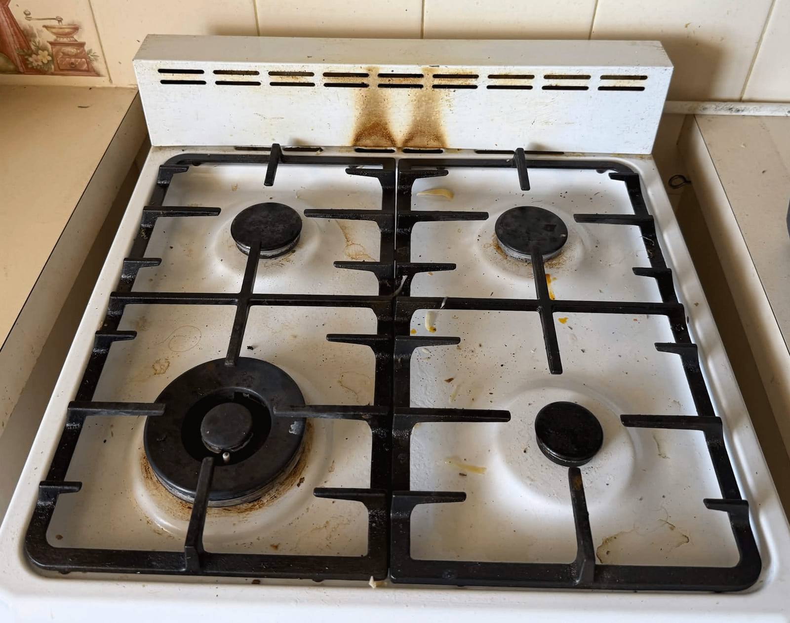 White four-burner gas cooktop with cast iron trivets and spills burnt onto the surface