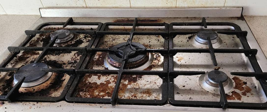 Gas stovetop with burnt spills across the enamel and heavy residue around the burner caps