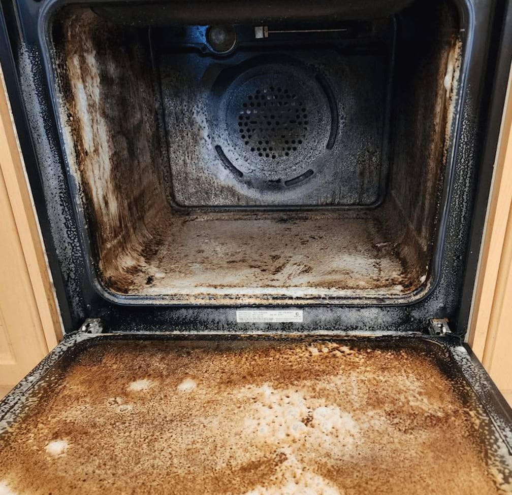 Oven with the door open, cavity walls and door tray thick with dark baked-on grease
