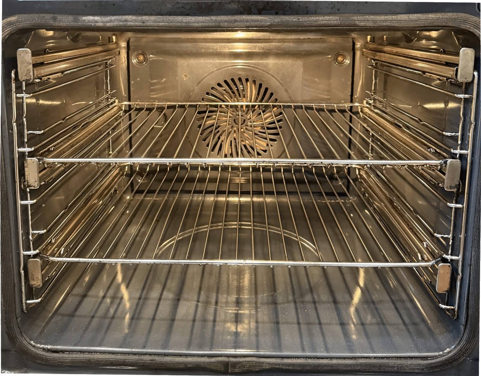 The same oven cavity after cleaning, with bright metal walls, a clear fan cover and clean chrome racks