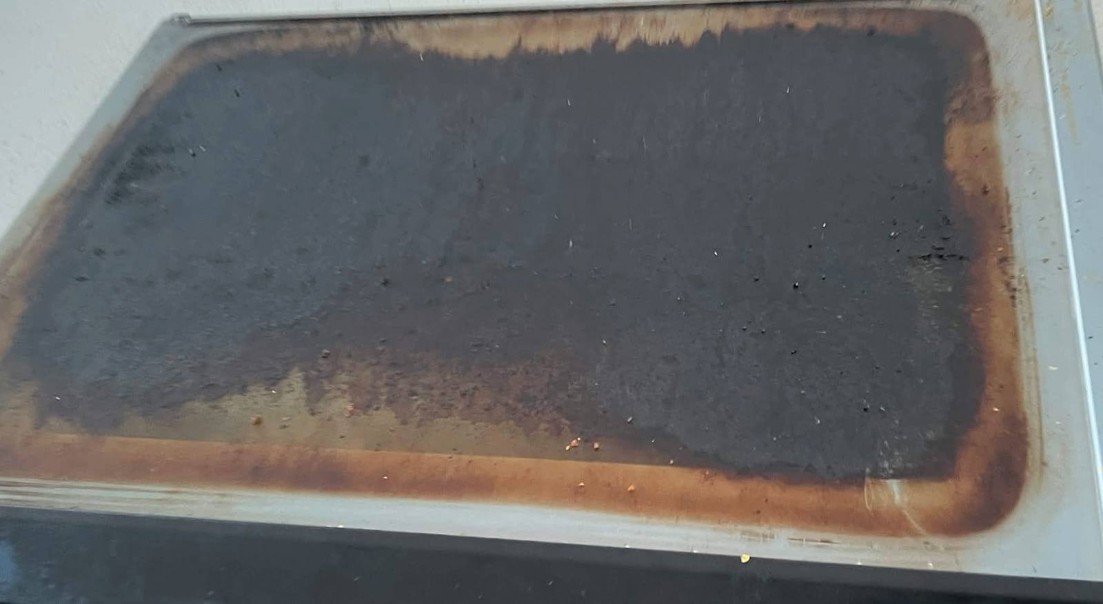Oven door glass panel removed and laid flat, stained opaque brown with baked-on residue