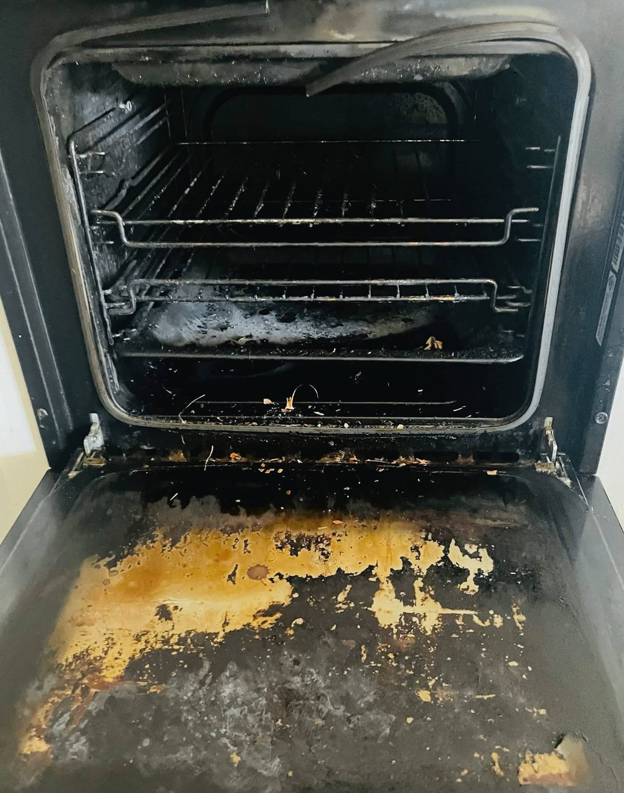 Oven interior with shelf runners in place and a door tray covered in burnt yellow and orange spills