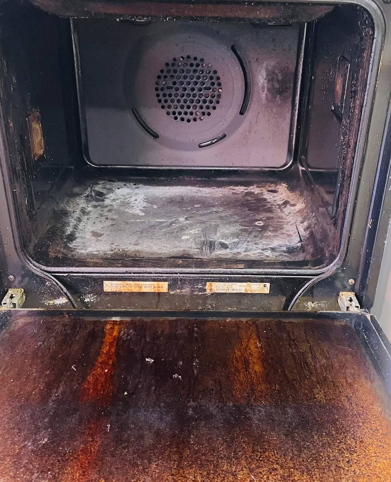 Oven cavity with a heavily soiled fan cover and a door tray stained deep rust brown