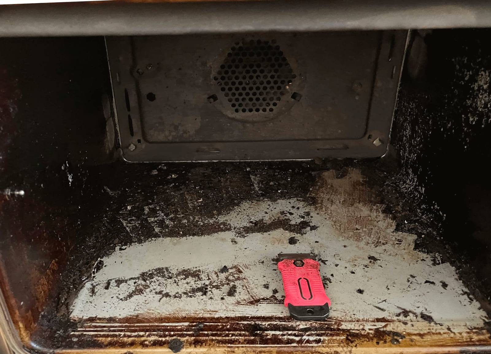Oven interior with chrome racks and a door tray heavily mottled with orange-brown grease