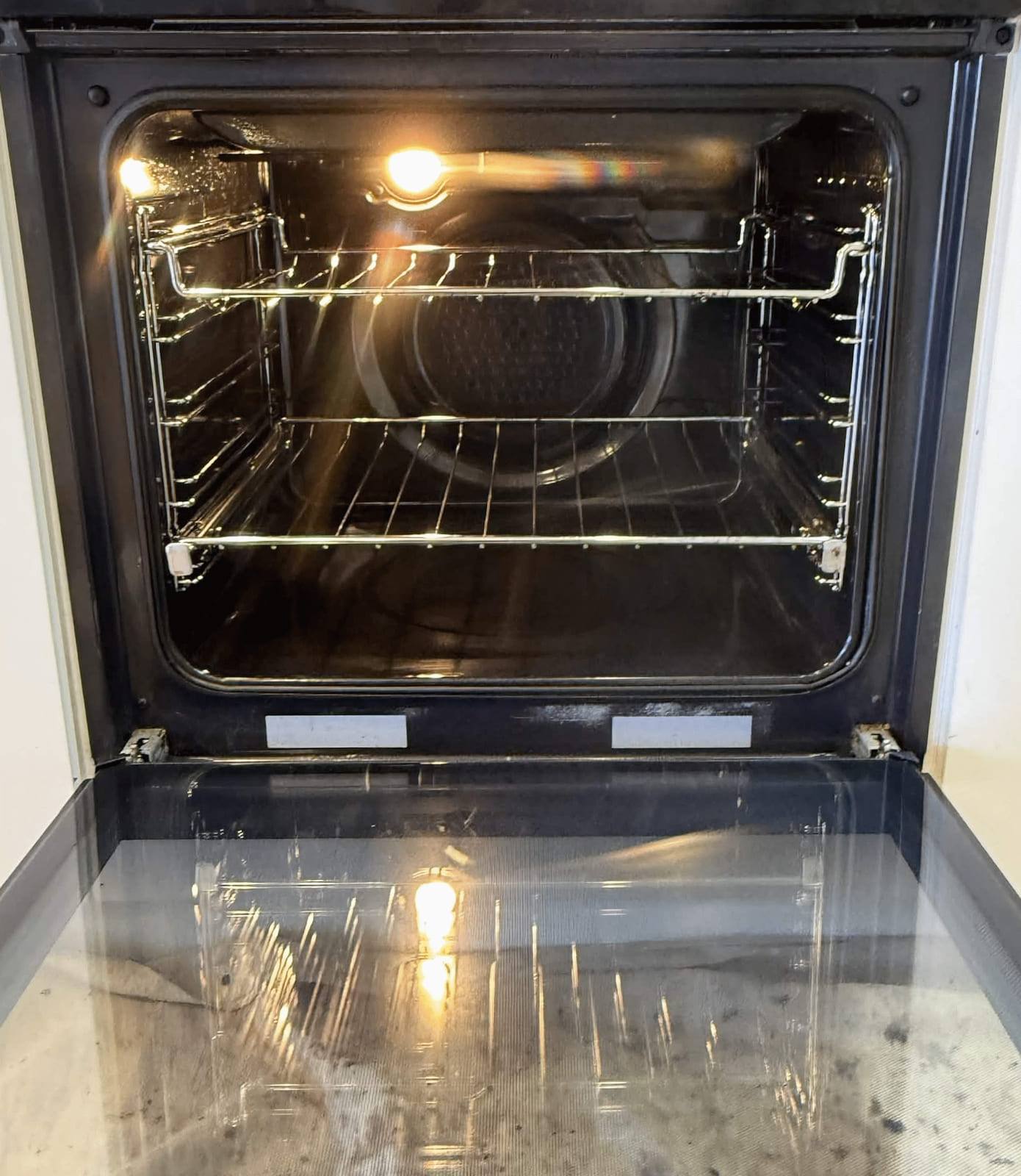 The same wall oven after cleaning, with clean racks, a clear fan cover and a spotless door tray